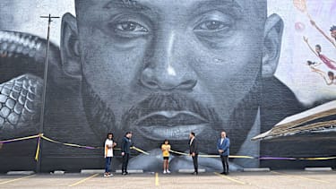 Ayla Rahmani (C) cuts the ribbon unveiling a new mural of the late Los Angeles Lakers basketball player Kobe Bryant, created by muralist Odeith and Los Angeles-based illustrator Nikkolas Smith, outside the headquarters of West Coast Trial Lawyers in Los Angeles, California, on August 24, 2022, "Mamba Day," an annual day of celebration of Kobe's career. - The unveiling is being held on "Mamba Day", the unofficial day of remembrance for Bryant, with 8 and 24 representing the numbers he wore during his career with the Lakers.
 - RESTRICTED TO EDITORIAL USE - MANDATORY MENTION OF THE ARTIST UPON PUBLICATION - TO ILLUSTRATE THE EVENT AS SPECIFIED IN THE CAPTION (Photo by Frederic J. BROWN / AFP) / RESTRICTED TO EDITORIAL USE - MANDATORY MENTION OF THE ARTIST UPON PUBLICATION - TO ILLUSTRATE THE EVENT AS SPECIFIED IN THE CAPTION / RESTRICTED TO EDITORIAL USE - MANDATORY MENTION OF THE ARTIST UPON PUBLICATION - TO ILLUSTRATE THE EVENT AS SPECIFIED IN THE CAPTION (Photo by FREDERIC J. BROWN/AFP via Getty Images)